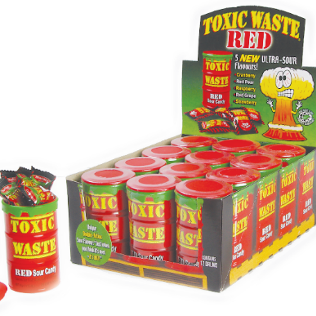 A display box of Toxic Waste Red Drum sour candies with individual packets visible. The box is colorful with a cartoon logo and graphics related to the product.