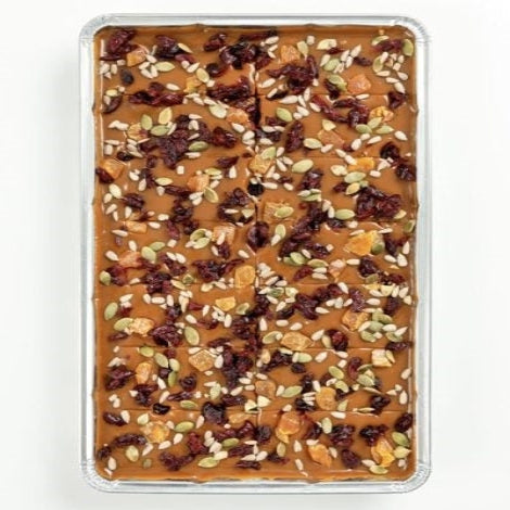 A tray of flapjacks with caramel chunks, cranberries, apricots, and seeds sprinkled on top.