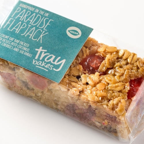 A packaged Traybakes Vegan Paradise Flapjack, featuring a chewy oat bar with glace cherries, sultanas and desiccated coconut.