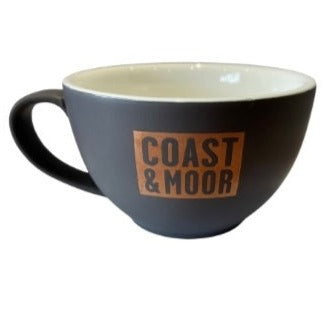 A slate gray cappuccino cup with the text 'COAST & MOOR' printed in orange and brown on the side.
