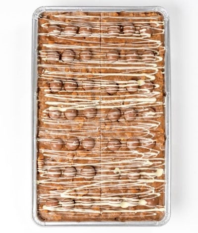 A large rectangular honeycomb biscuit cake with chocolate pieces and white chocolate drizzle on top, cut into portions.