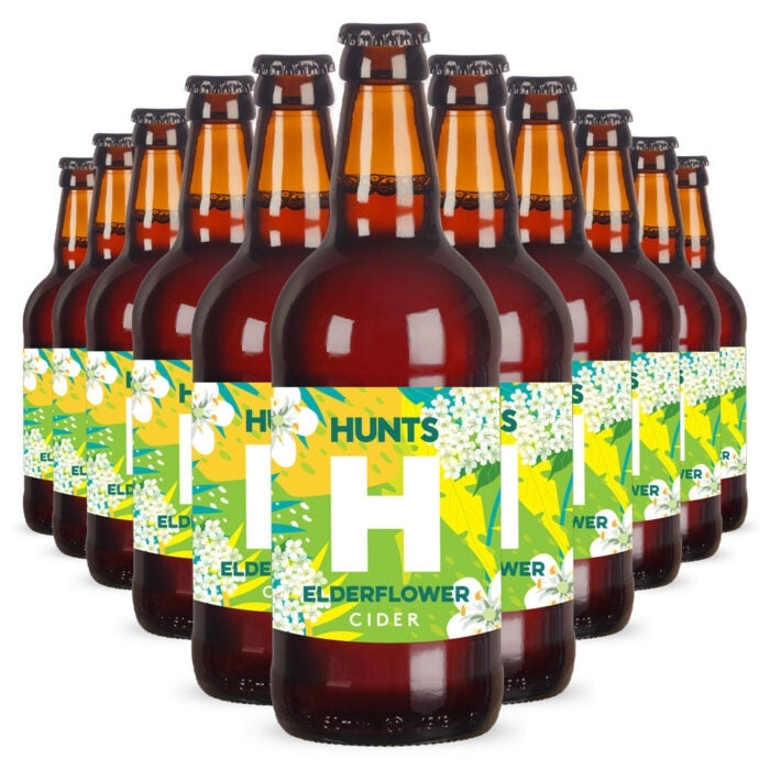 A pack of Hunt's Elderflower Cider bottles arranged in a fan shape against a white background. The bottles are dark brown glass with amber necks and feature a bright green and yellow label with white elderflower illustrations.