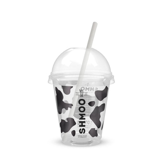 A clear plastic cup with a black and white cow print pattern, a clear dome lid, and a white straw. The cup features the vertical brand name 'SHMOO' in black.