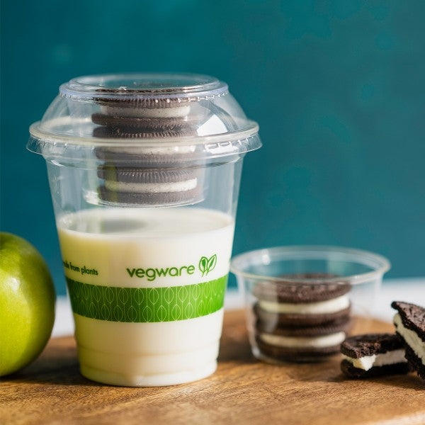 Vegware container with milk and cookies on a wooden surface.